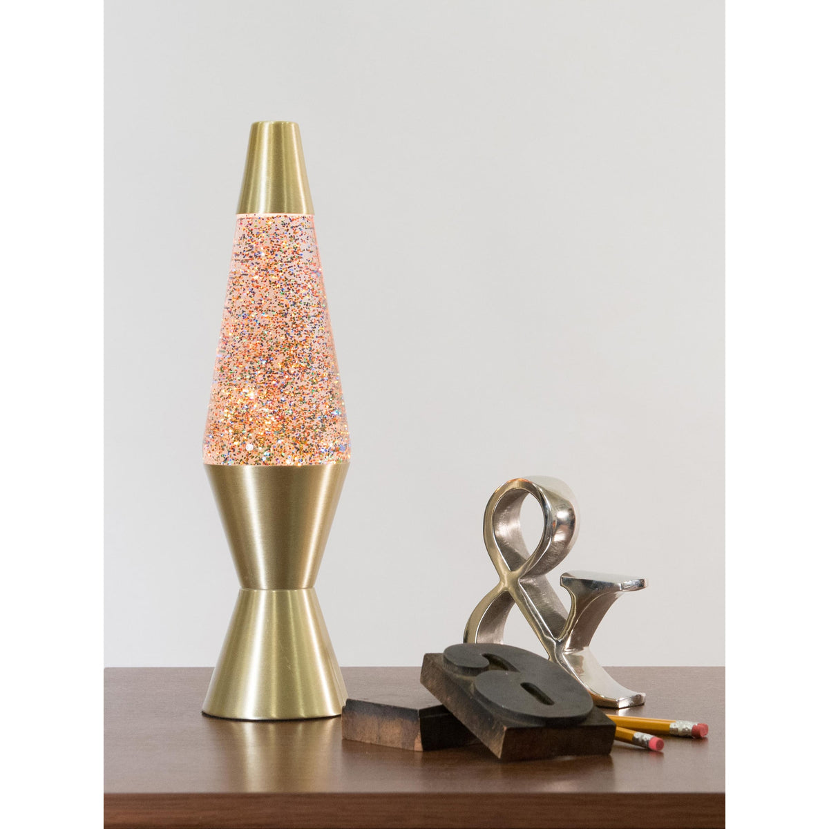 14.5” LAVA® Lamp Rainbow Glitter – Clear/Gold on a table with knick knacks